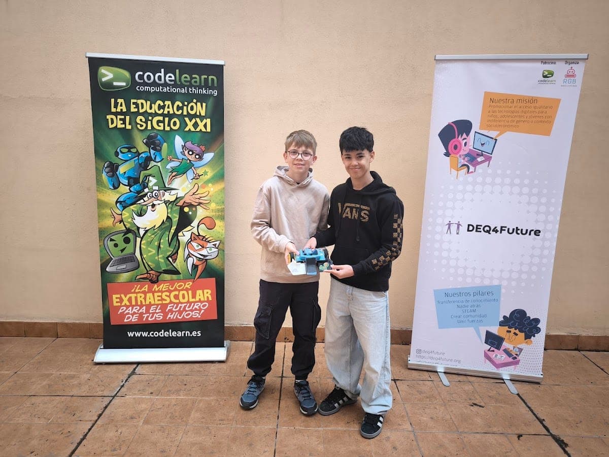 Dos participantes de la RGB 2025 en Zaragoza sostienen su robot ante los carteles de Codelearn y DEQ4Future