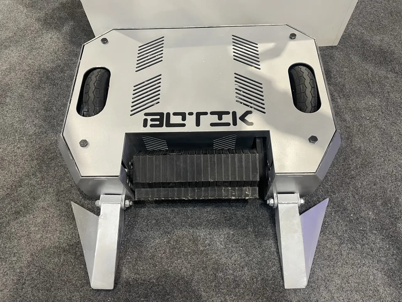 Robot de combate metálico visto desde arriba, con un tambor delantero y dos cuñas