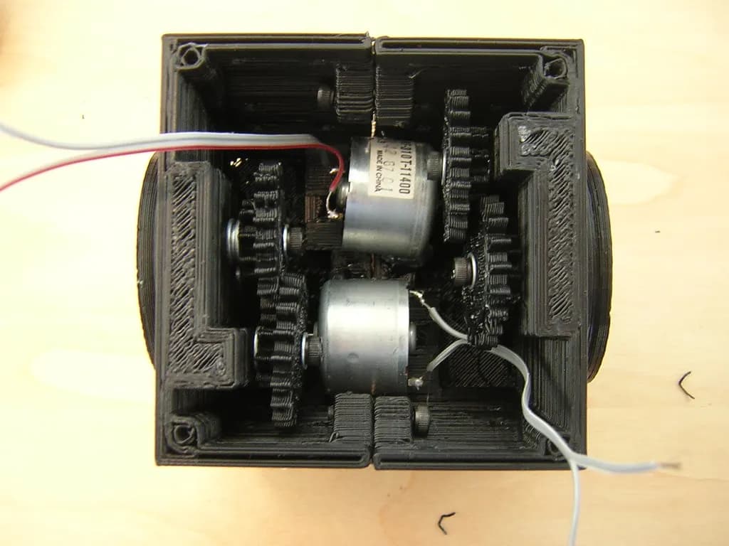 Chasis pequeño de plástico impreso en 3D abierto, con motores, engranajes y cableado visibles